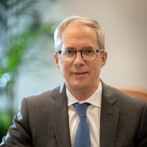 Head shot photo of a white man with glasses and a blue tie in front of a soft focus background.