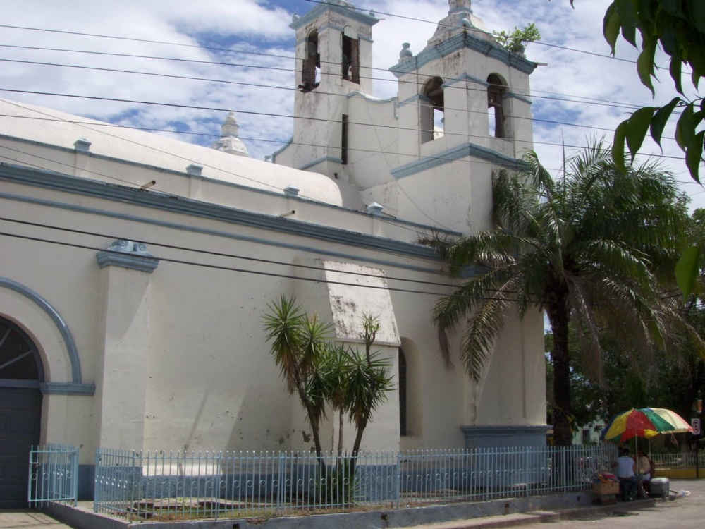 Photo of a white-walled cathedral, with power lines and palm trees next to it.