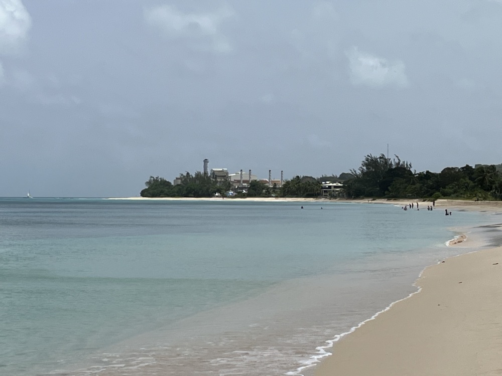 A photo of a power plant on the other side of a beautiful white sand beach.
