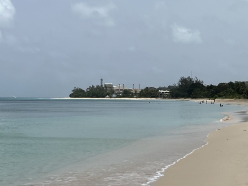 A photo of a power plant on the other side of a beautiful white sand beach.