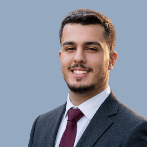 A headshot image of a man in a suit smiling at the camera.