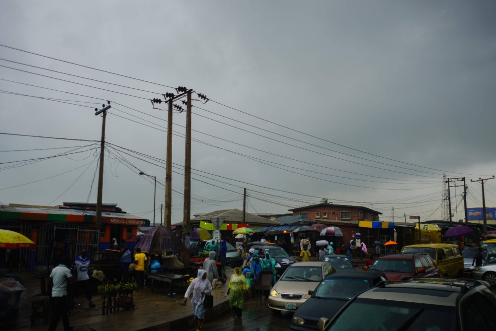 Photo of a busy market on a rainy day, with power lines prominently showing against the cloudy sky.